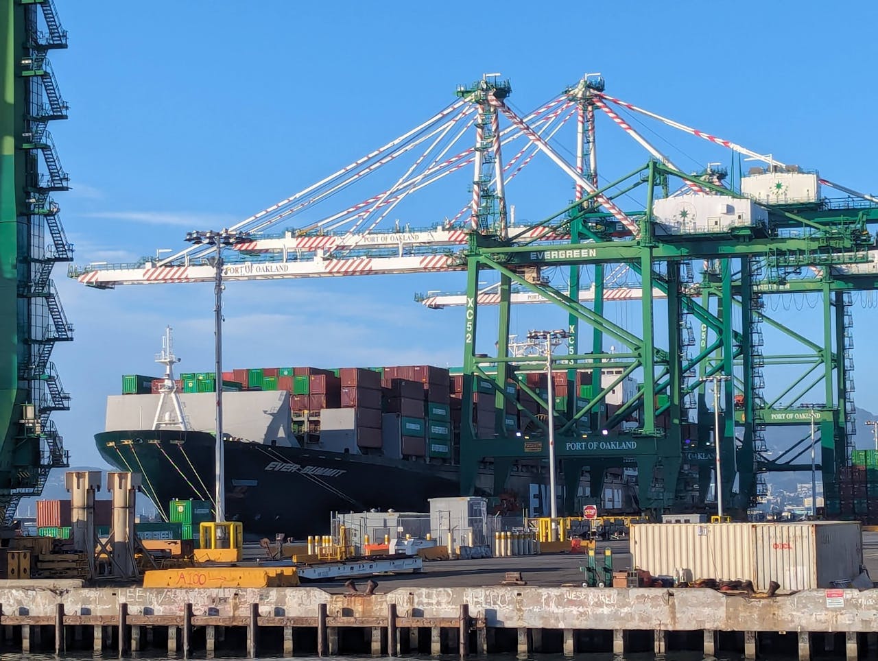 Container cargo ship docked at Port of Oakland with cranes for loading and unloading.